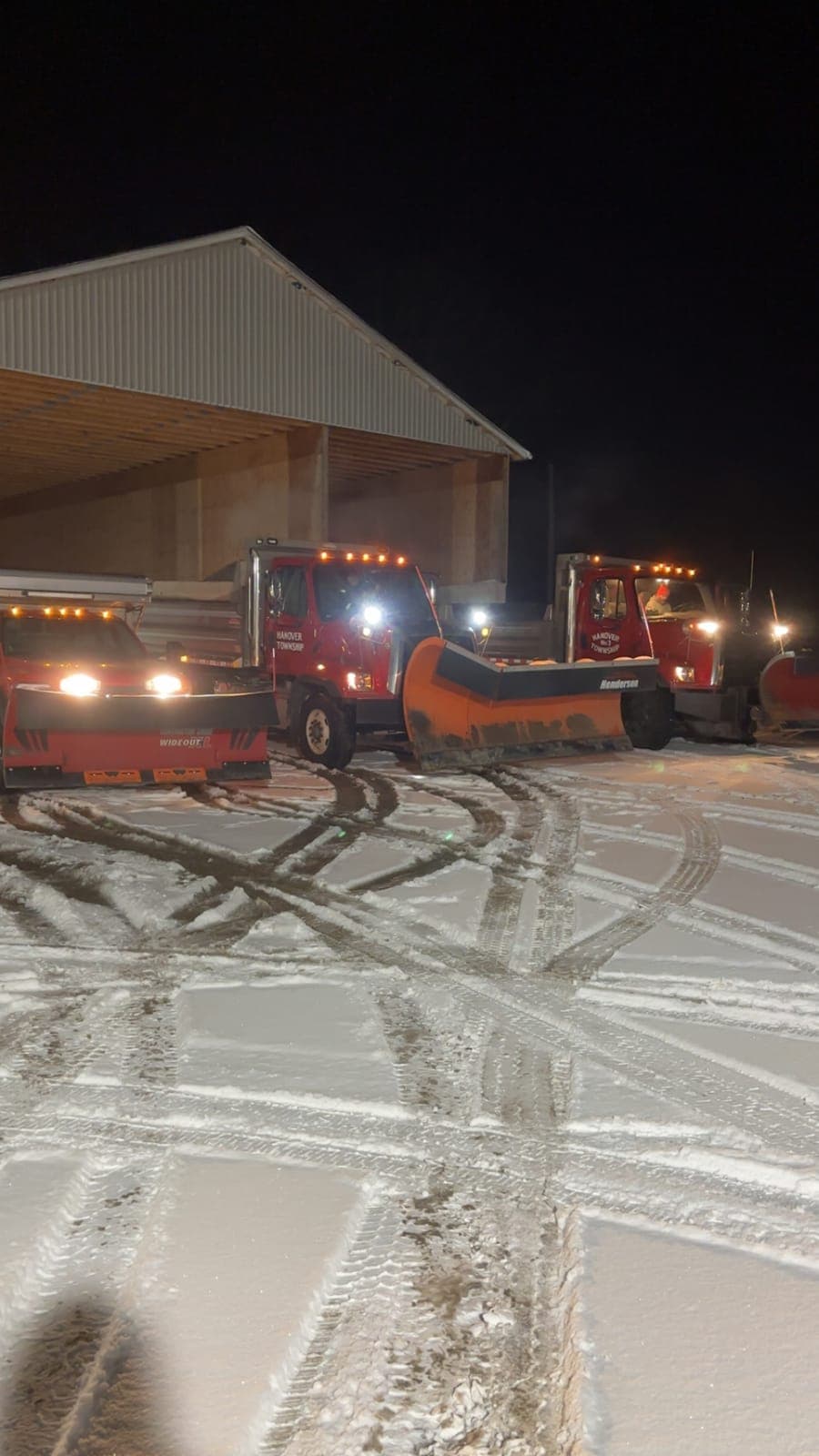 Three Hanover Township plow trucks lined up outside the garage at night with their lights on